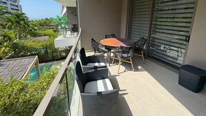 En balkon med et bord og stole, en ventilator i loftet og udsigt til havet og bygninger.