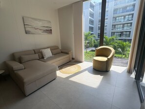 A modern living room with a beige sectional sofa, a round rug, and a single armchair. A large window offers a view of a cityscape and greenery. - 2-bedroom apartment in peaceful Cartagena de Indias with beach access and pool (Cartagena de Indias)