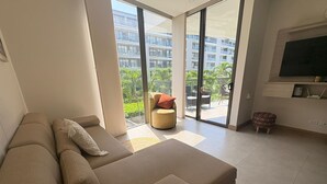 En moderne stue med en stor sofa, et lille rundt bord og et fjernsyn monteret på væggen.