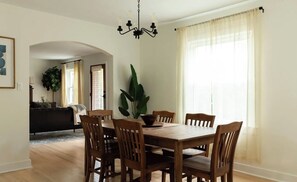Un comedor con mesa y sillas de madera, una araña y una planta grande.