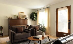 Una sala de estar con un sofá, una mesa de centro, una estantería, una planta en maceta y una puerta con ventanal.