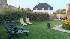 Un jardin avec une pelouse, deux chaises longues, une petite table et un mur en briques.