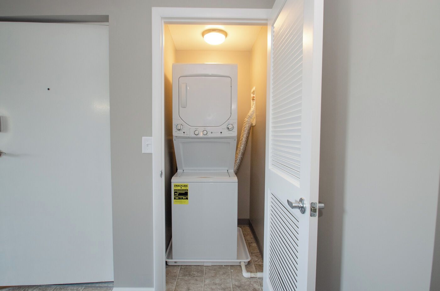 A laundry room with a front-loading washer and dryer, a door with a handle, and a light fixture above the appliances.