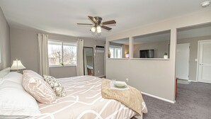 A bedroom with a bed, a ceiling fan, a window, and a door.