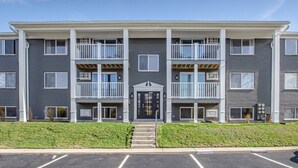 A multi-story apartment building with a central entrance, balconies, and a parking lot in front.
