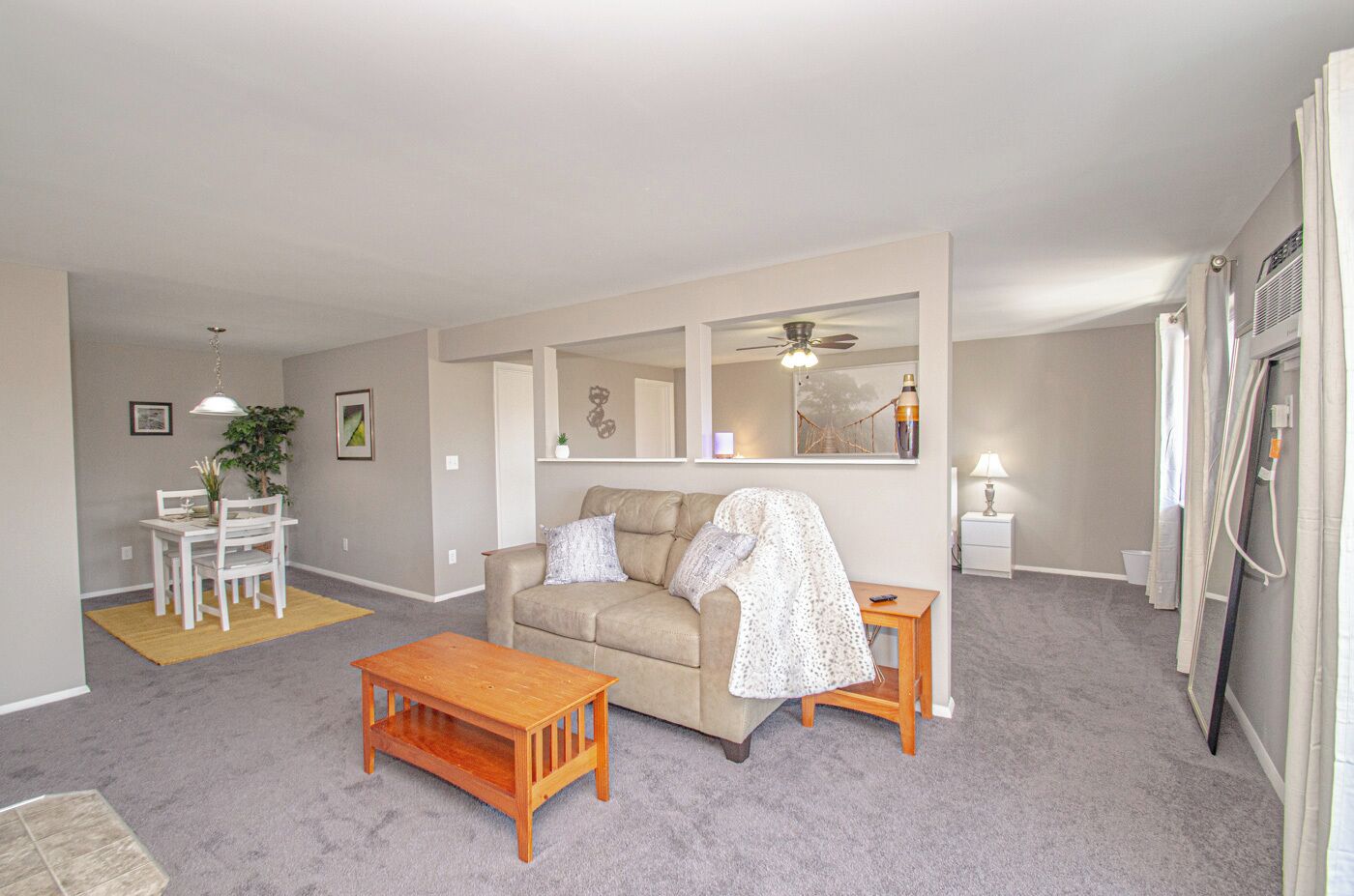 Un salon avec un canapé beige, une table basse en bois, une table à manger avec des chaises et une petite table d’appoint.