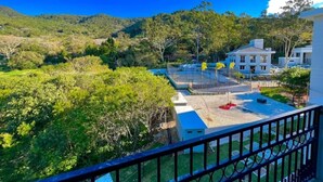 A view from a balcony overlooking a landscaped area with a building, trees, and a clear sky. - Apartment in Summer Park (Florianópolis)