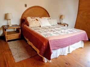 Une chambre à coucher avec un lit en bois, une literie à motifs floraux, deux tables de chevet avec des lampes et une tête de lit en osier.