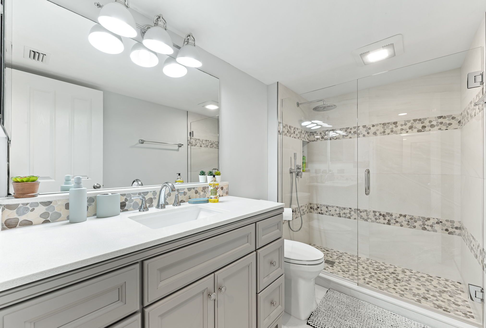 A modern bathroom with a large mirror, dual sinks, and a glass-enclosed shower area.