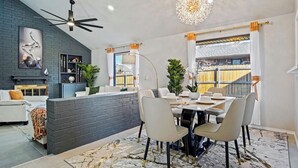 Een moderne keuken met een donkere, met baksteen beklede spatwand, een eethoek met een ronde tafel en stoelen, en een groot raam met gordijnen.