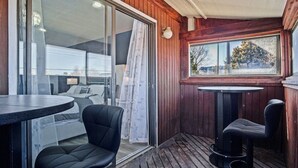 Een houten terras met een schuifdeur die leidt naar een slaapkamer, een ronde tafel en twee stoelen.