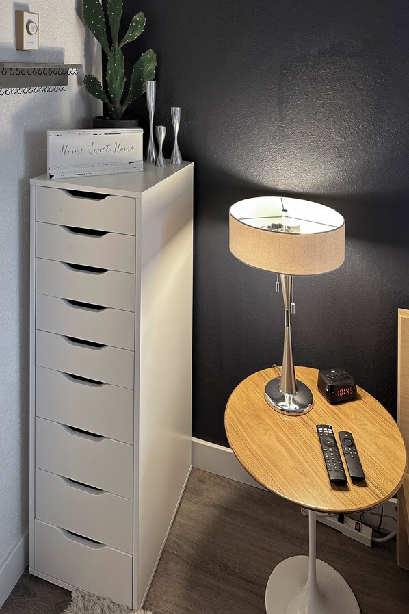 A modern room with a white storage unit, a round wooden table with a lamp, two remote controls, and a digital clock. - Red Pine Retreat at Canyons Village (Park City)