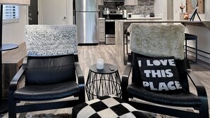 A modern kitchen with a stainless steel refrigerator, a microwave, and a stove. There are two chairs with fluffy throw pillows and a black and white checkered ottoman. - Red Pine Retreat at Canyons Village (Park City)
