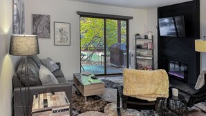 A living room with a sofa, coffee table, and a fireplace. There is a sliding glass door leading to an outdoor area with a barbecue grill. - Red Pine Retreat at Canyons Village (Park City)