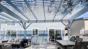 Ein möblierter Patio mit Korbmöbeln, einem Holztisch und einem überdachten Sitzbereich.
