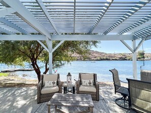 A covered outdoor seating area with wicker chairs and a table, overlooking a body of water. - All-american Escape, Riverfront! WB3 (Parker Dam)