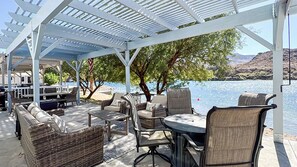An outdoor patio with wicker furniture and a table, overlooking a body of water. - All-american Escape, Riverfront! WB3 (Parker Dam)
