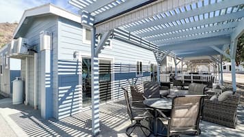 A covered outdoor patio with a dining table and chairs, a grill, and a water heater.