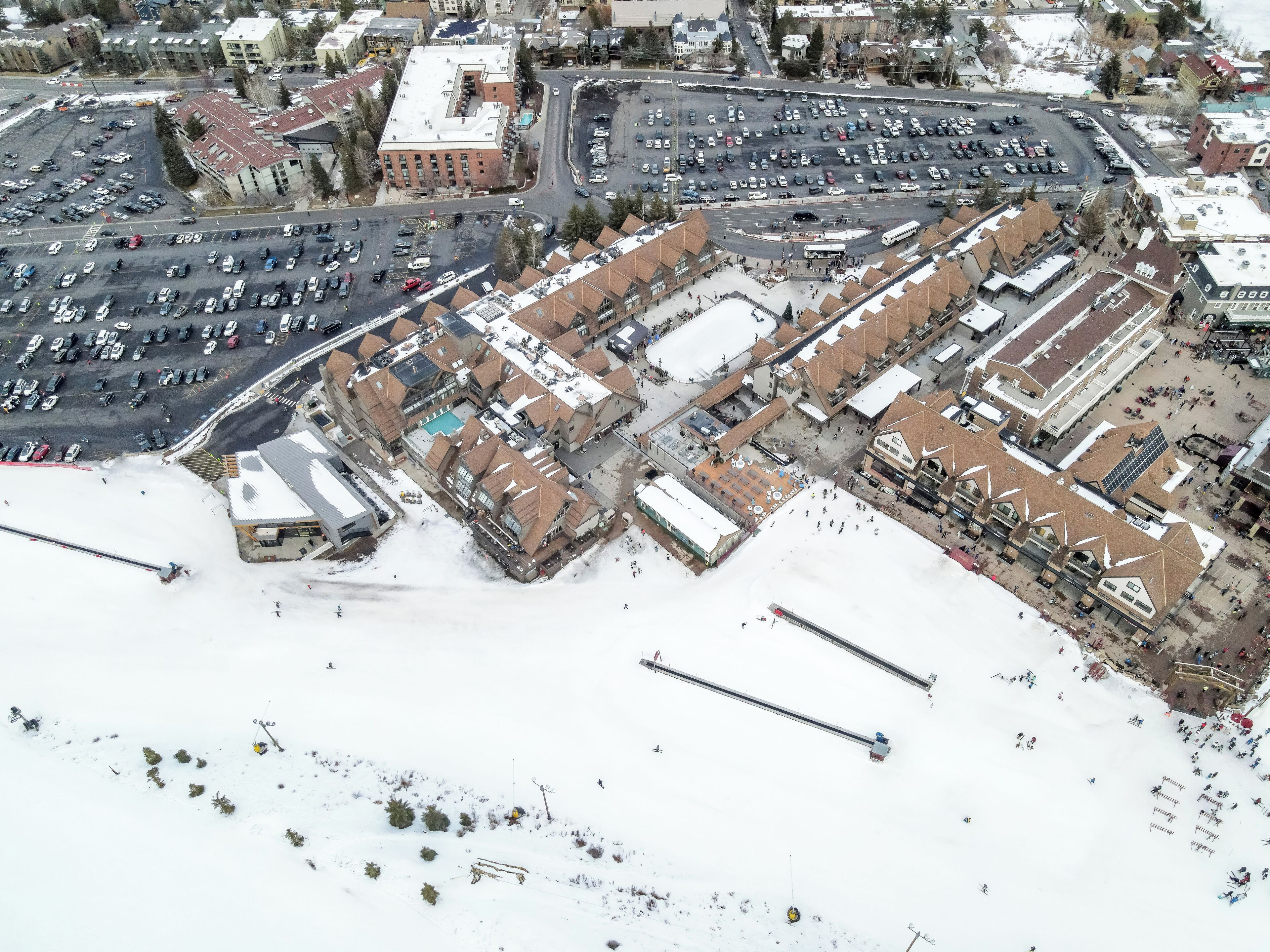An aerial view of a commercial area with parking lots, buildings, and a snowy landscape.
