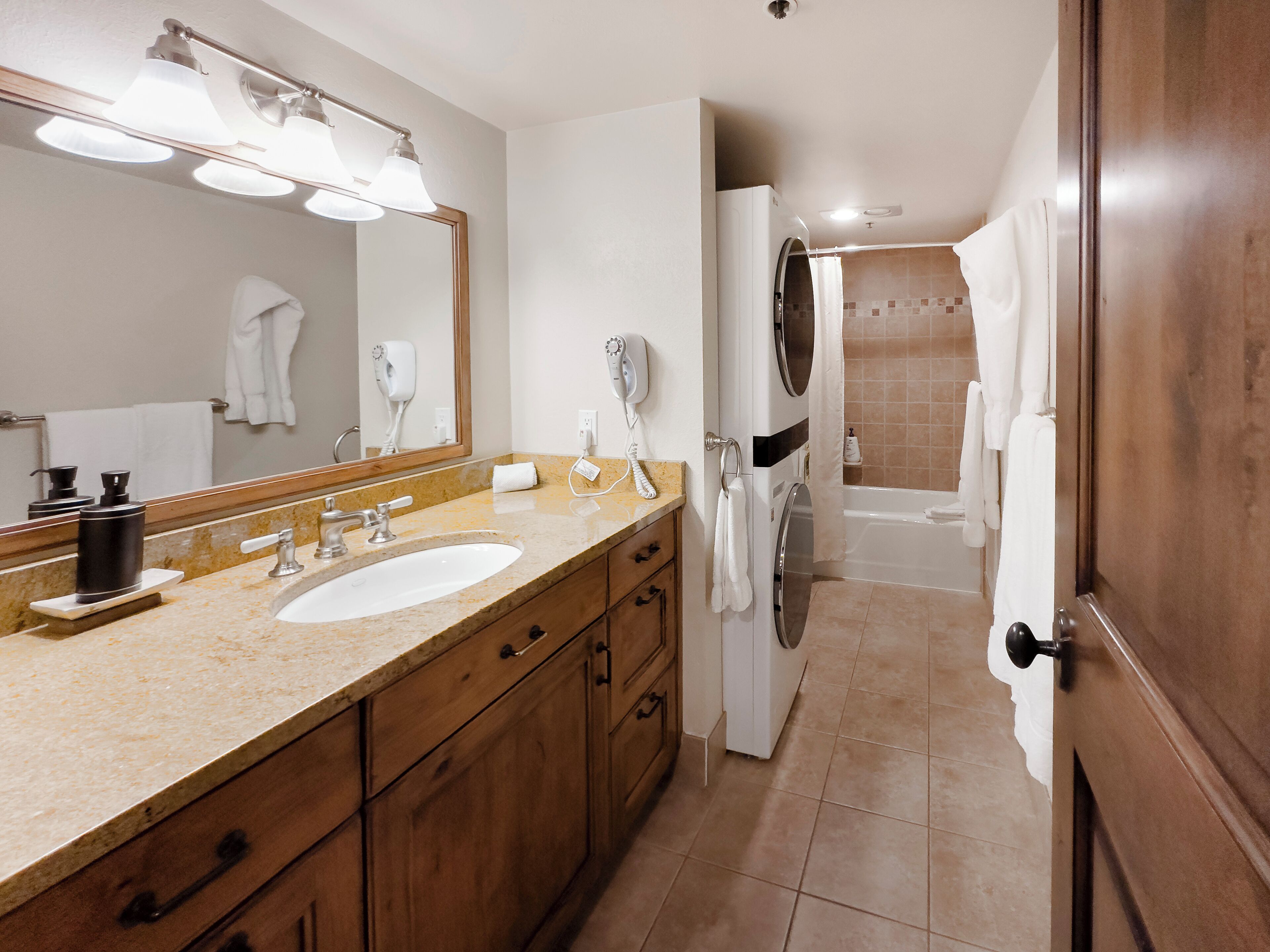 A bathroom with a double sink vanity, a large mirror, a hairdryer, and a shower area.
