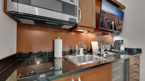 Une cuisine moderne équipée d’un four à micro-ondes en acier inoxydable, d’un four encastré, d’un évier et d’un téléviseur à écran plat fixé au-dessus du plan de travail.