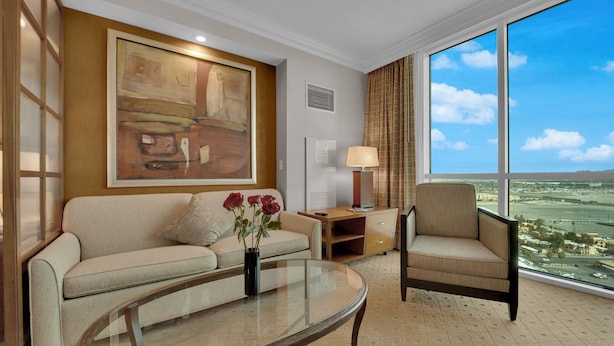 Une chambre d’hôtel moderne avec une grande fenêtre, un canapé, un fauteuil, une table basse en verre et un tableau au mur.