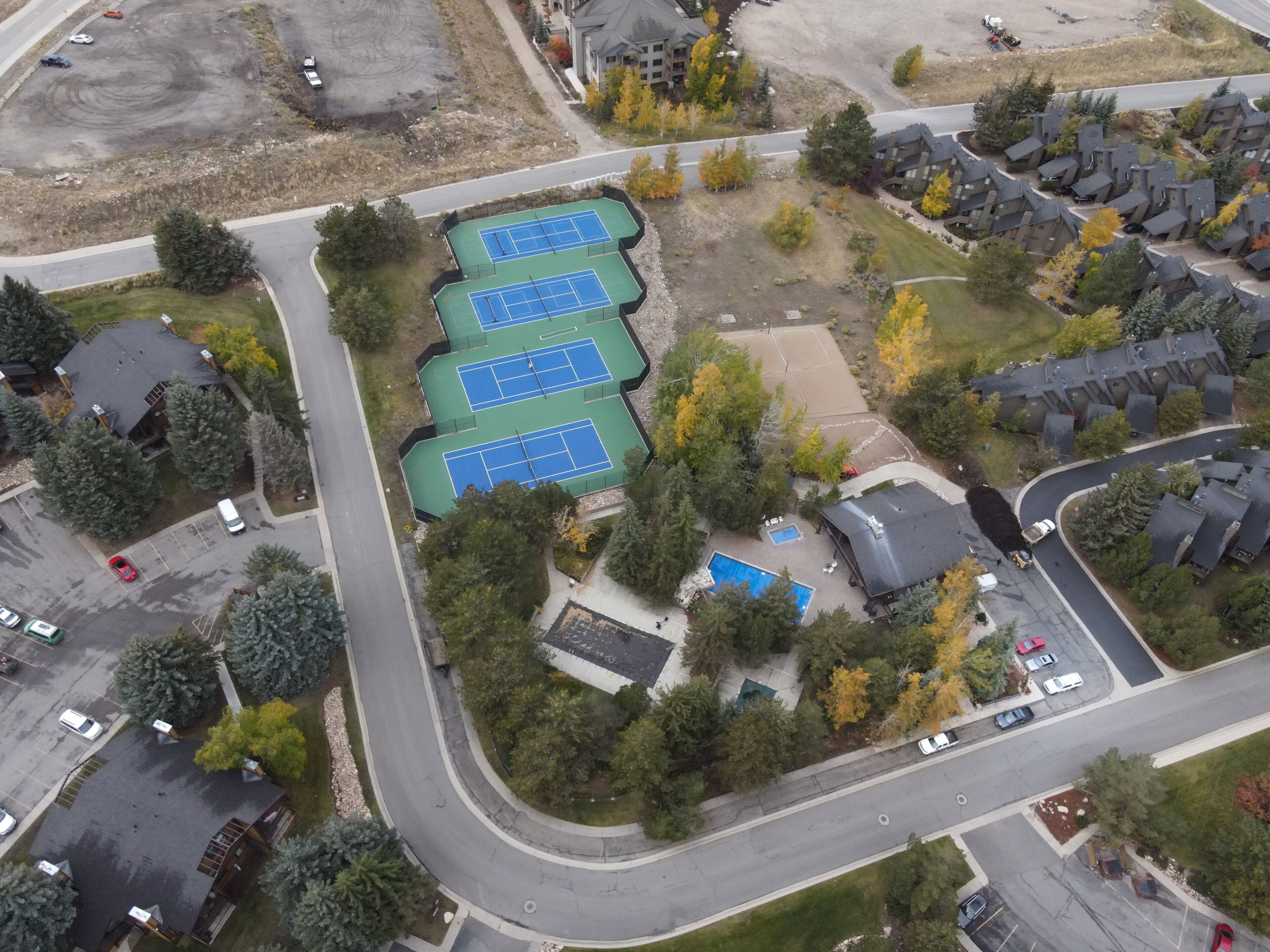 An aerial view of a residential area with a tennis court, a swimming pool, and houses.