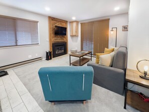 A modern living room with a fireplace, a sofa, a blue armchair, and a small table. - Relaxing Canyons Condo Free Shuttle Ride To Lift (Park City)