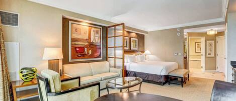 A hotel room with a bed, a sofa, a coffee table, and a painting on the wall.