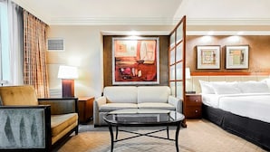 Una camera d'albergo con un letto, una poltrona, una sedia, un tavolo e opere d'arte alle pareti.