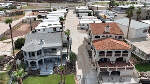A coastal residential area with multiple two-story houses, a paved walkway, and a small dock extending into the water. - Gorgeous Hacienda on the River! Private Dock! (Parker)