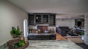 A spacious living area with a large dark leather sofa, a coffee table, and a kitchen area with dark cabinets and a marble countertop. - Gorgeous Hacienda on the River! Private Dock! (Parker)