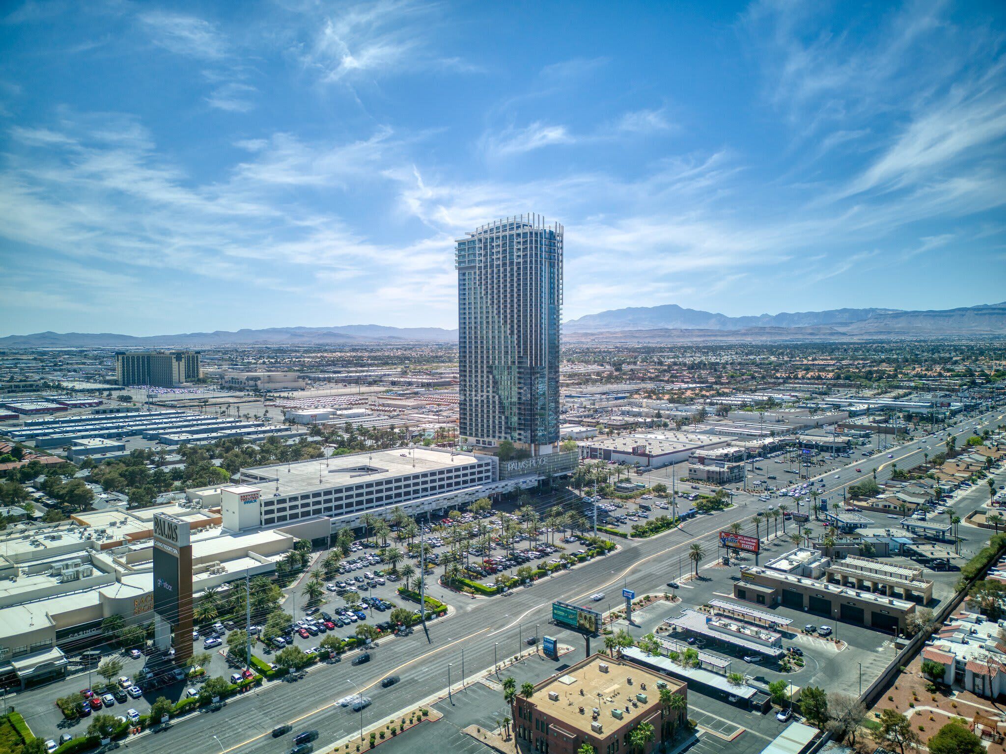 A high-rise building with a modern glass facade, surrounded by a parking lot and a busy road.