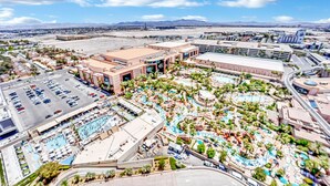 Un hotel grande con varias piscinas, estacionamiento y vistas a montañas distantes.