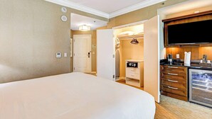 Ett hotellrum med en stor säng, en rymlig klädkammare, ett litet kök och en tv som är monterad på väggen.