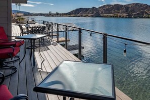 Une terrasse avec des sièges extérieurs, une table en verre et une vue sur une rivière et des montagnes.