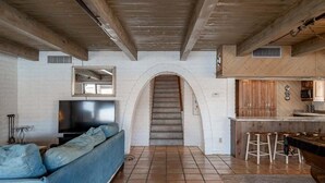 Ein Wohnzimmer mit einer Couch, einem Fernseher und einer Treppe, die in einen Küchenbereich führt.