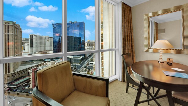 A hotel room with a large window offering a city view, a round table with a lamp, and a chair. - Mirai MGM (Las Vegas)