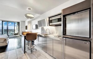 A modern kitchen with stainless steel appliances, a large window, and a city view. - Luxurious Sub-penthouse Studio Balcony Access (Las Vegas)