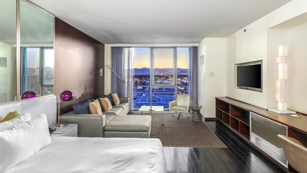 A modern hotel room with a large bed, a sofa, a TV, and a balcony with a city view. - Luxurious Sub-penthouse Studio Balcony Access (Las Vegas)