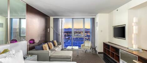 Una habitación de hotel moderna con una cama grande, un sofá, un televisor y un balcón con vistas a la ciudad.