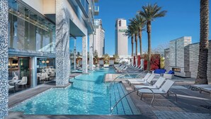 A pool area with lounge chairs, a restaurant, and tall buildings in the background. - Luxurious Sub-penthouse Studio Balcony Access (Las Vegas)