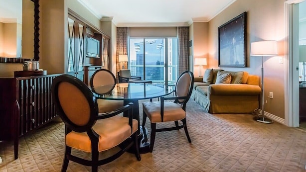 A hotel room with a dining table, chairs, a sofa, a TV, and a large window with a city view. - MGM Signature 1BR Balcony 06721 (Las Vegas)