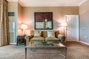 A hotel room with a sofa, a glass coffee table, a lamp, a painting on the wall, and a door. - MGM Signature 1BR With Balcony 08714 (Las Vegas)