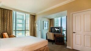 Una camera d'albergo con un letto grande, una scrivania con televisore e vista sulla città attraverso ampie finestre.