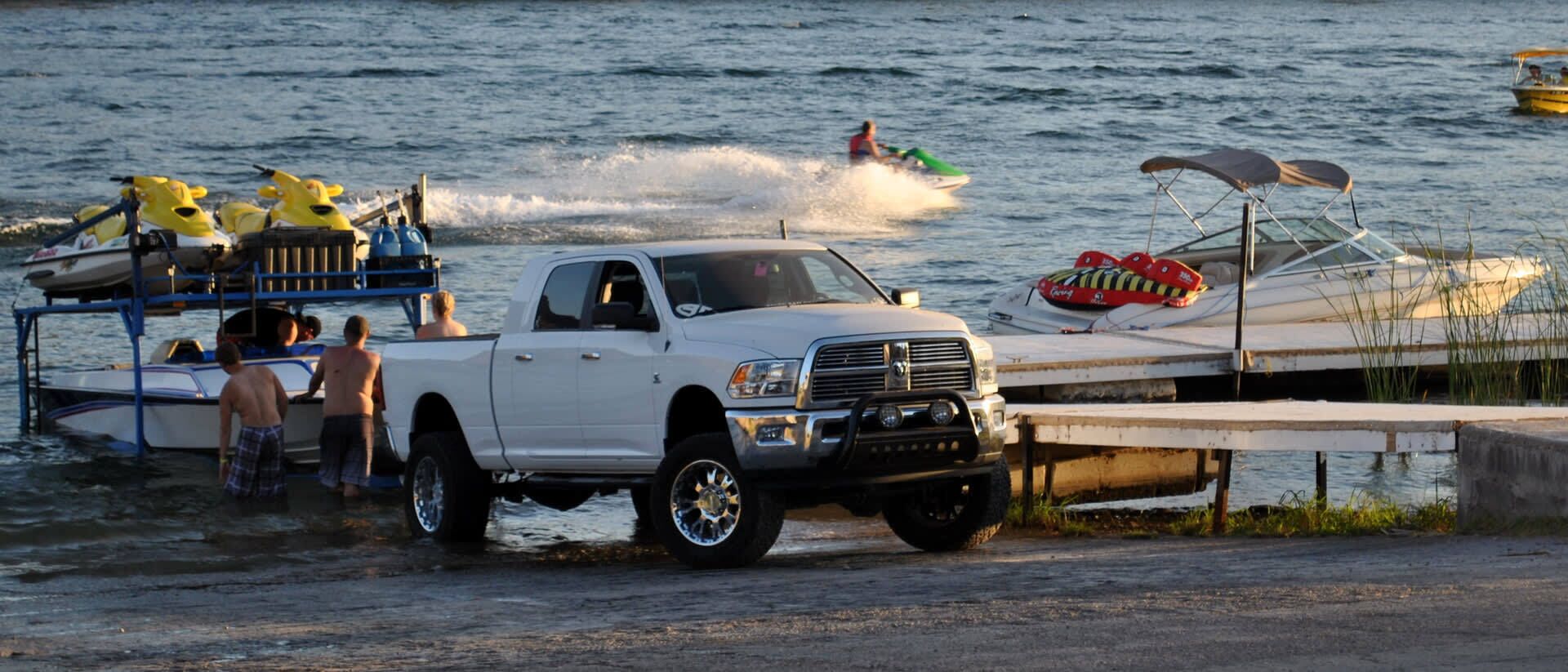 A white pickup truck parked by a dock with a boat trailer attached.