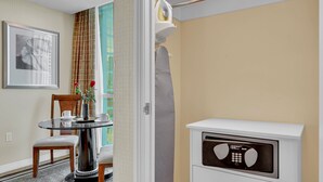 Una habitación de hotel con una mesa redonda de cristal, dos sillas, un minibar blanco y un cuadro en la pared.