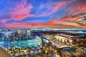 A hotel with a large outdoor pool, a well-lit parking area, and a view of the cityscape at dusk. - Kintsugi Retreat-condo-balcony-stripview (Las Vegas)