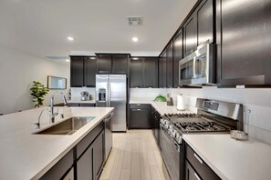 A modern kitchen with stainless steel appliances, dark cabinetry, and a light-colored countertop. - Casa Niva (Las Vegas)