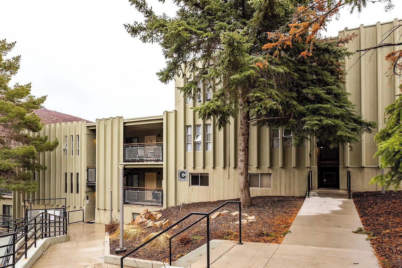 A modern building with a central staircase, a covered outdoor area, and a tree in front.
